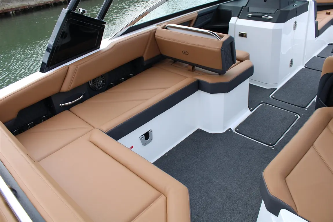 Luxury boat interior featuring tan leather seating, gray carpet, and a small monitor, against a water backdrop.